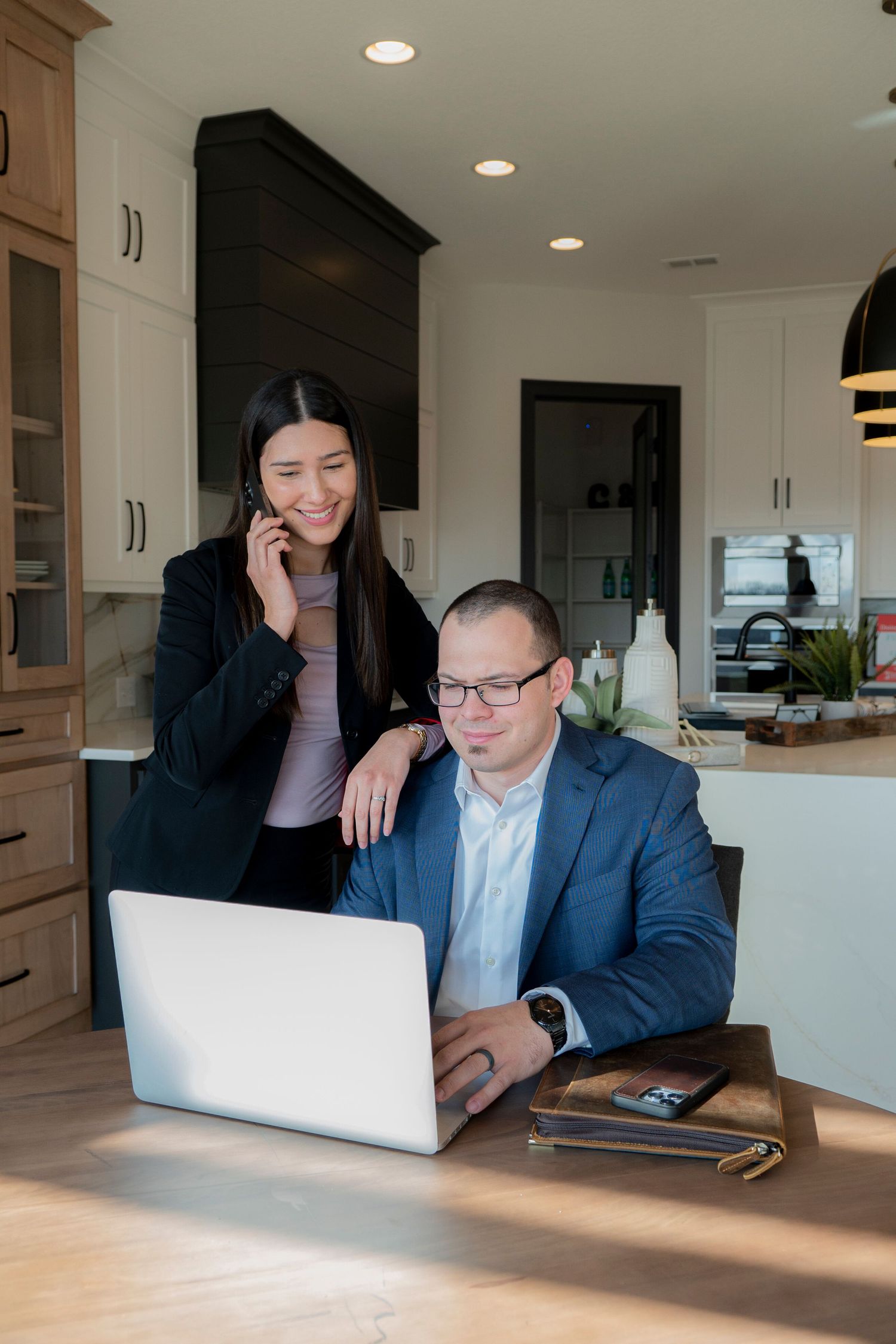 Branding Portrait of 2 real estate agents at a table with one on the phone and the other on a computer smiling