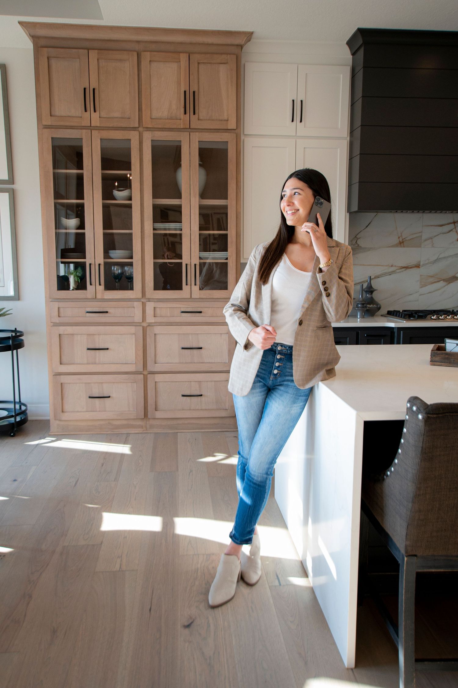 Branding portrait of a real estate agent leaning against a kitchen island smiling and looking away while talking on the phone