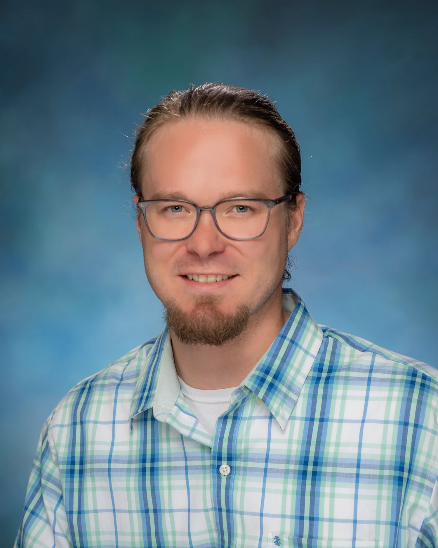Business headshot of a man in a blue plaid collared shirt on a blue background