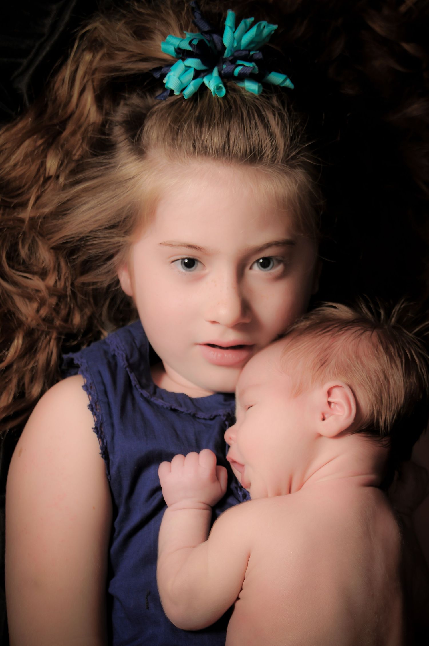 Portrait of young girl holding her baby brother on her chest with a black background with dramatic lighting