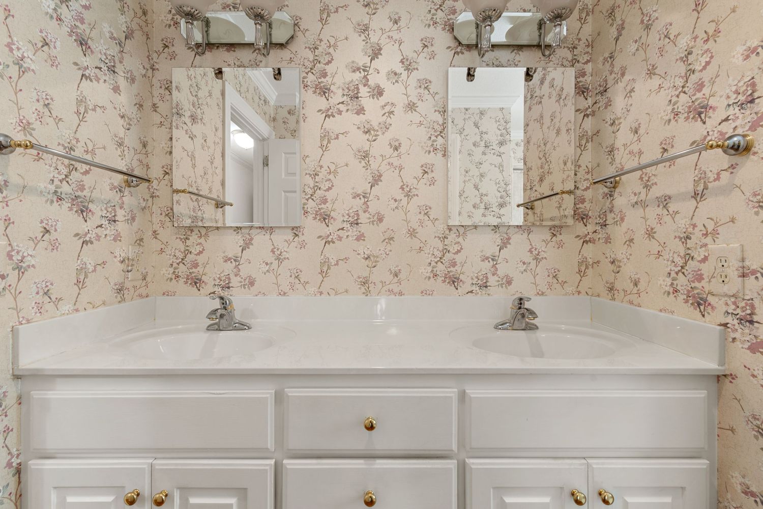 Double sink white vanity with floral wallpaper and dual mirrors in an elegant bathroom.