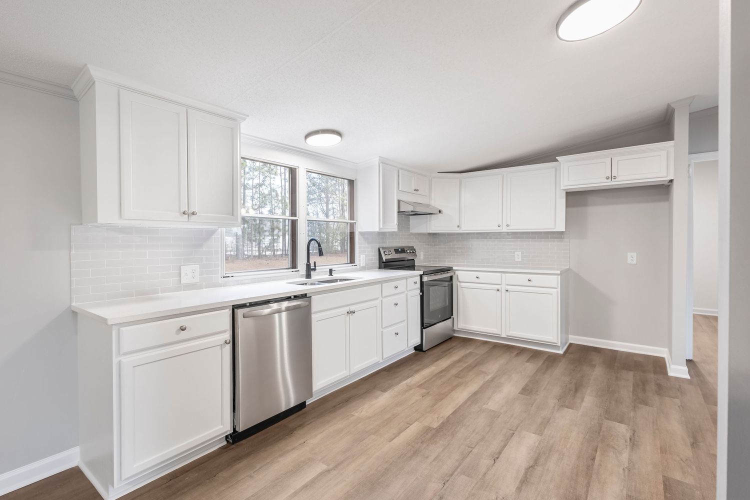 Modern white kitchen with shaker cabinets, quartz countertops, and luxury vinyl plank flooring in a bright open space.