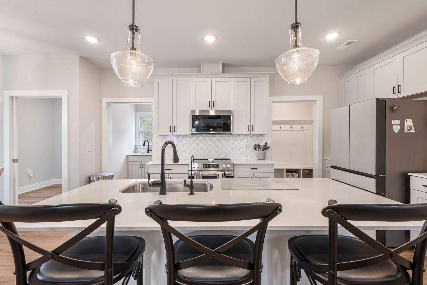 Modern white kitchen with marble island, black barstools, pendant lights, stainless appliances, and subway tile backsplash.