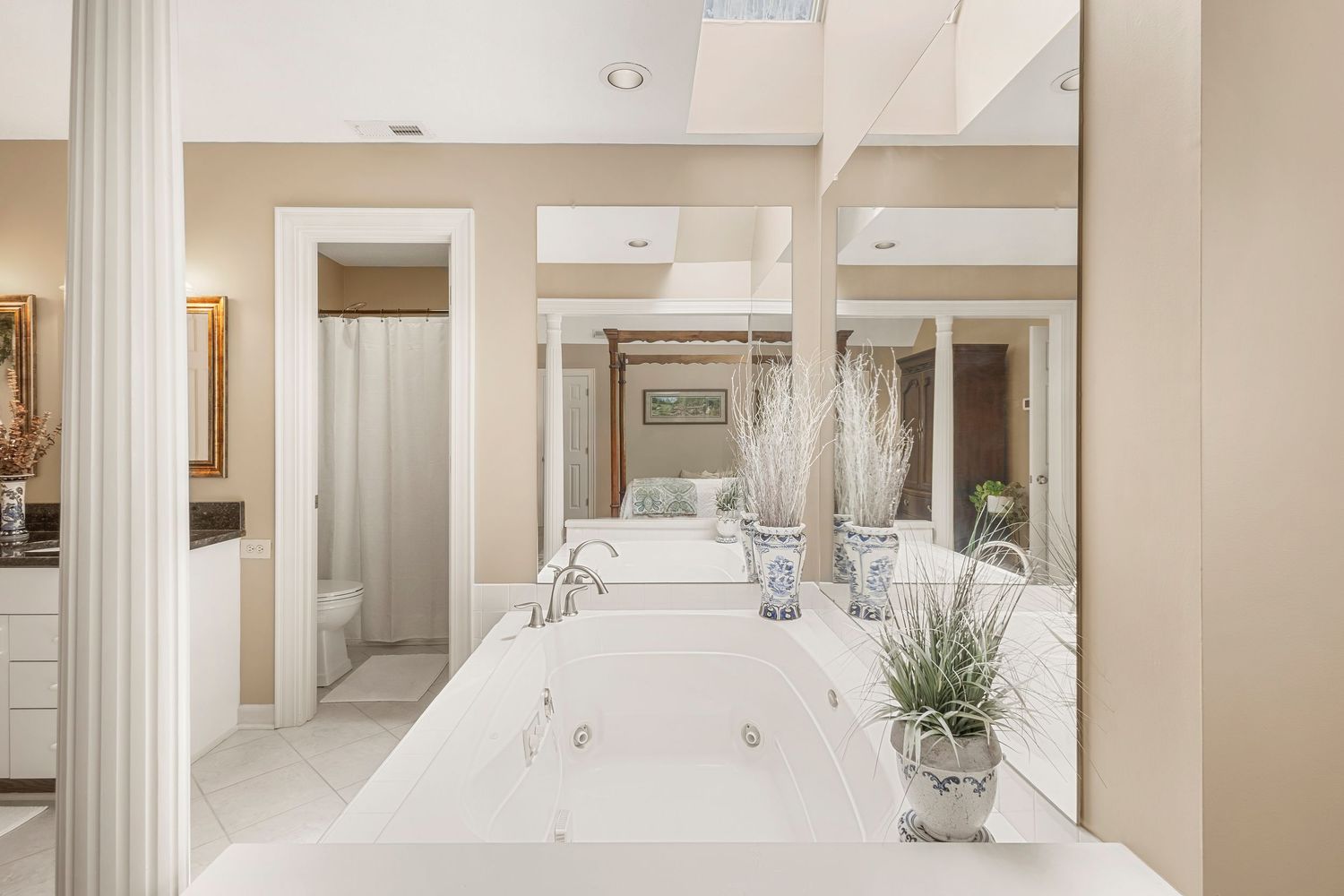 Luxurious white master bathroom featuring a jetted soaking tub, mirrored walls, and elegant decorative plants.