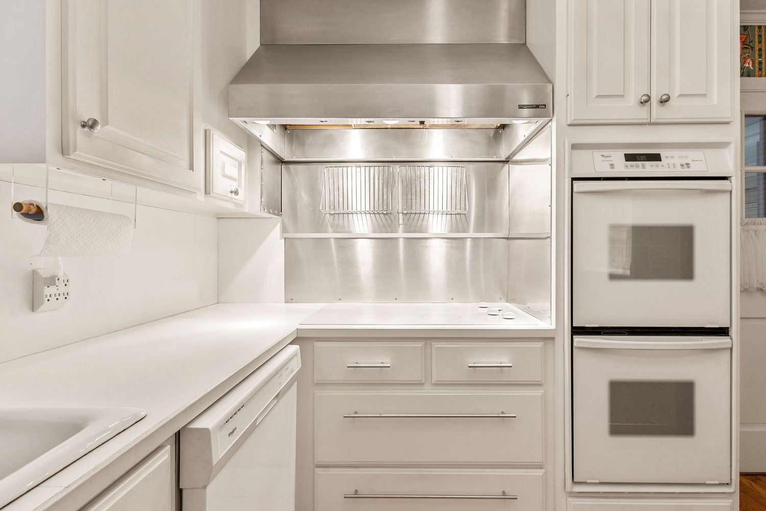 White kitchen with double wall ovens, stainless steel range hood, white cabinetry, and quartz countertops.