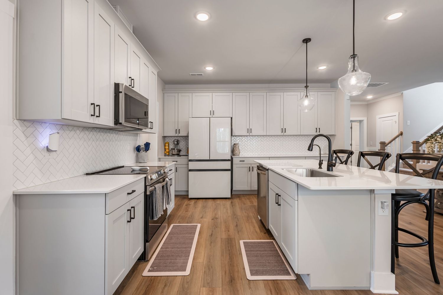 Modern white kitchen with stainless steel appliances, quartz island, pendant lights, and hardwood floors.