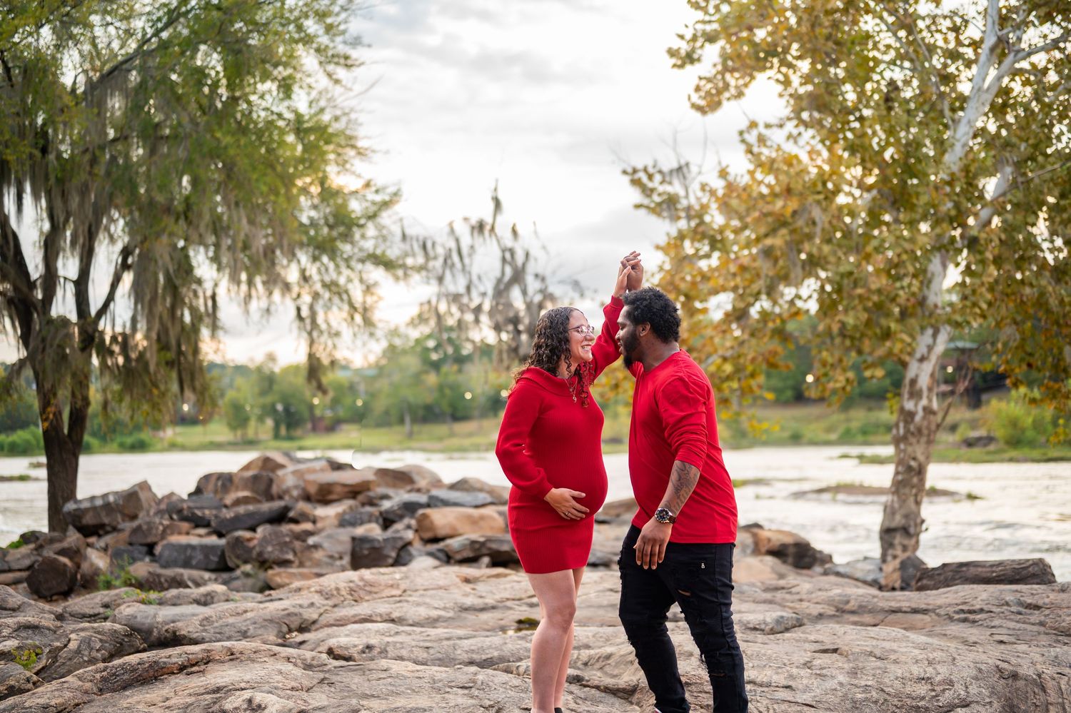 Family wearing red outfits stands together on rocky shore during fall photoshoot.