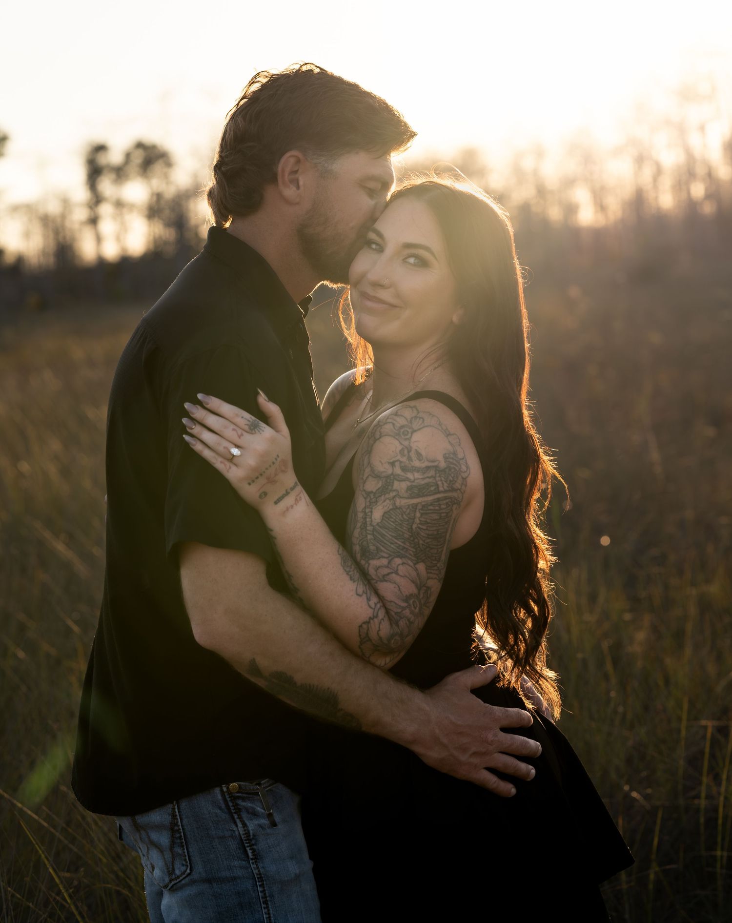 Romantic couple embraces in a golden field at sunset with dramatic backlighting.