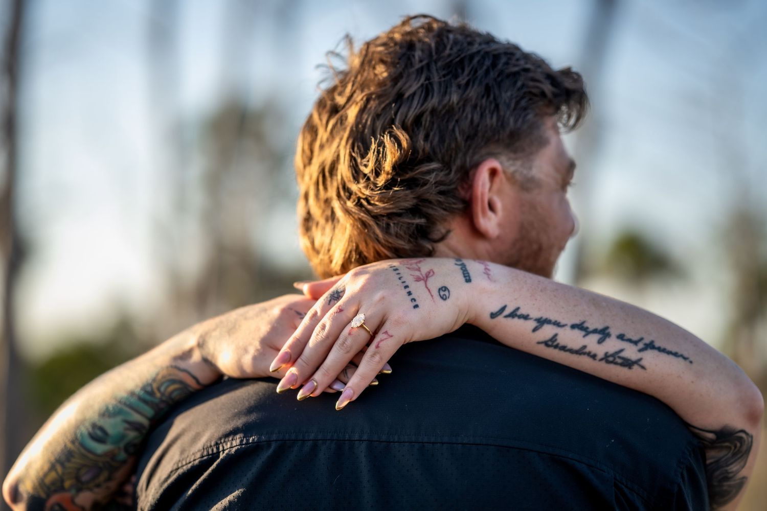 A couple embraces in a romantic moment outdoors during golden hour with a blurred natural background.
