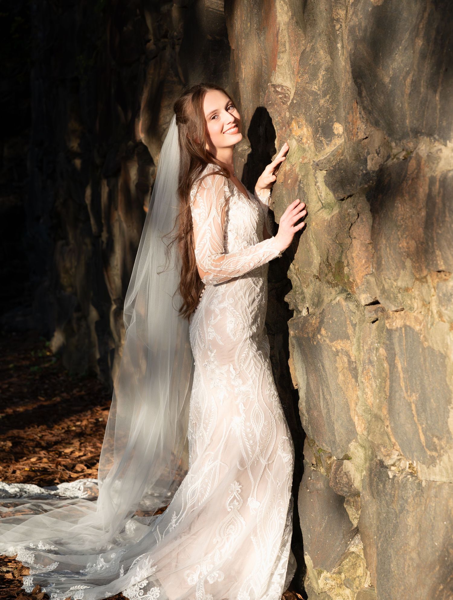 Moody bridal portraits against stone wall showing intricate details of lace wedding dress.