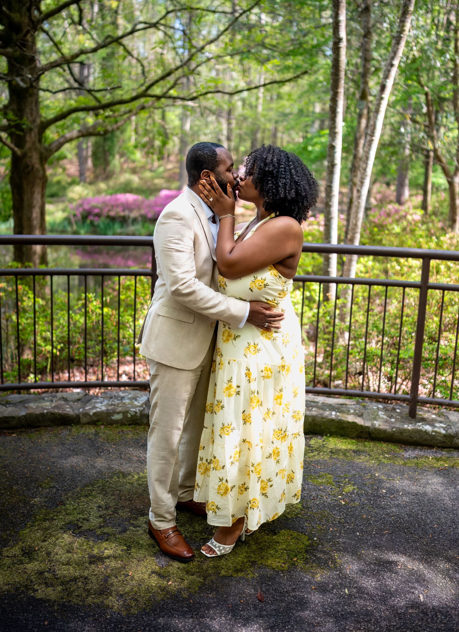 A couple sharing a tender kiss outdoors in a serene garden with blooming azaleas in the background.