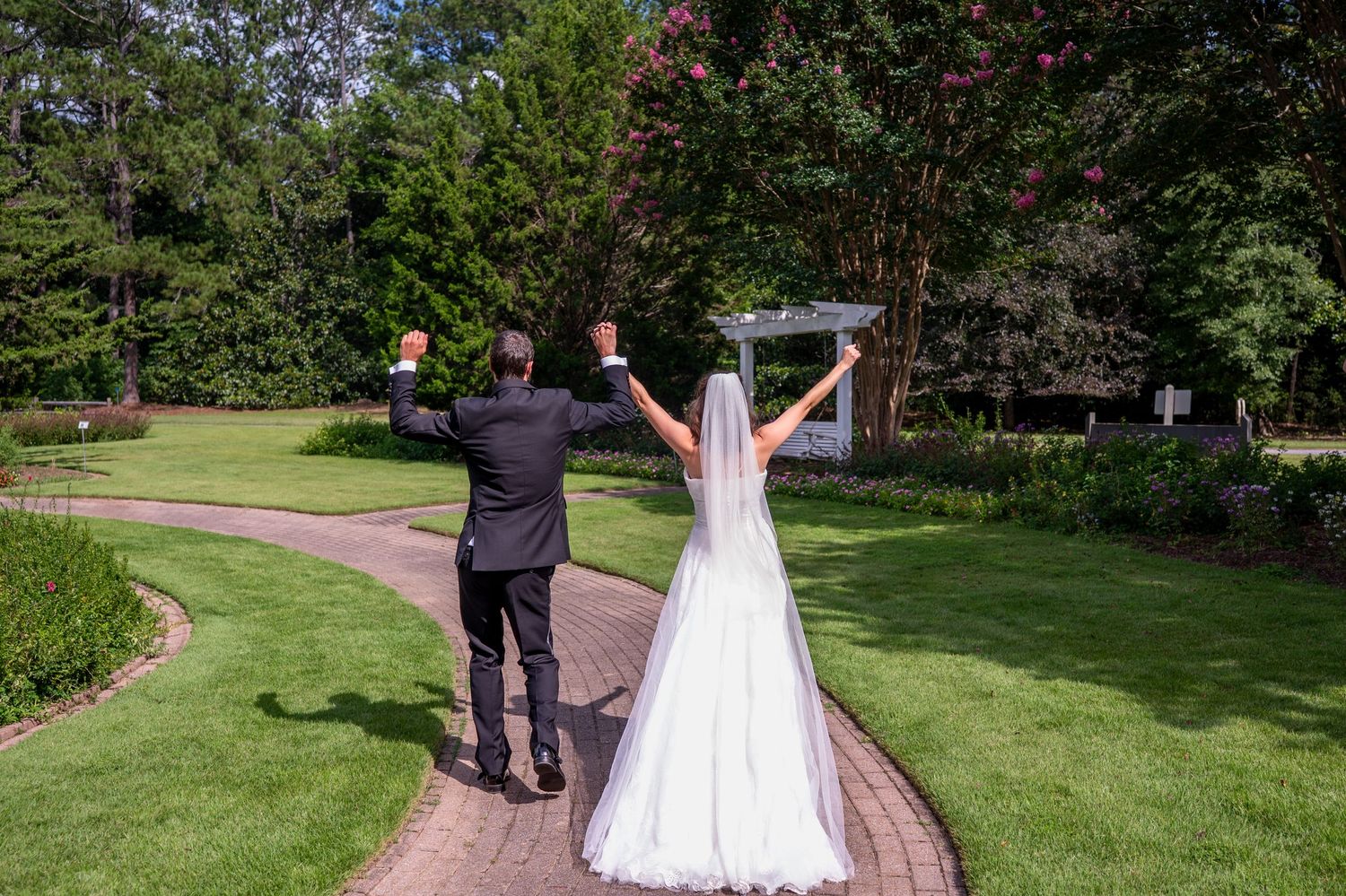 A couple walks away holding hands across a lush green lawn during a wedding celebration.