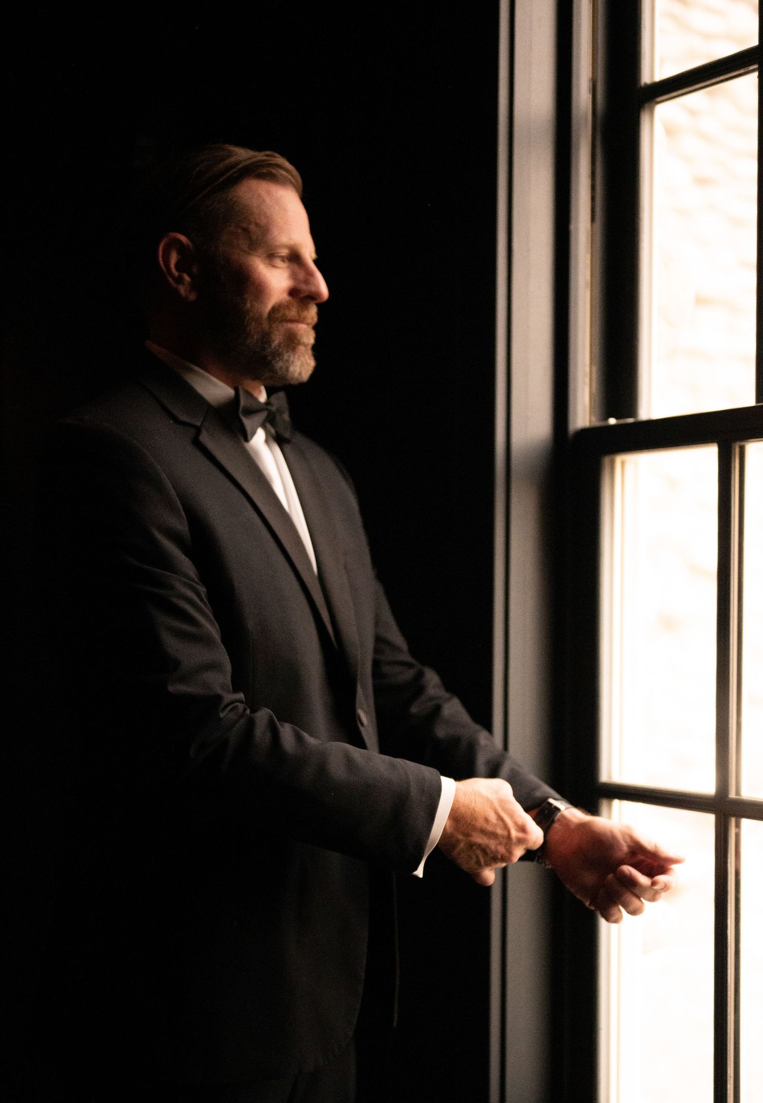 Dramatic silhouette of a male groom in formal attire by a bright window.