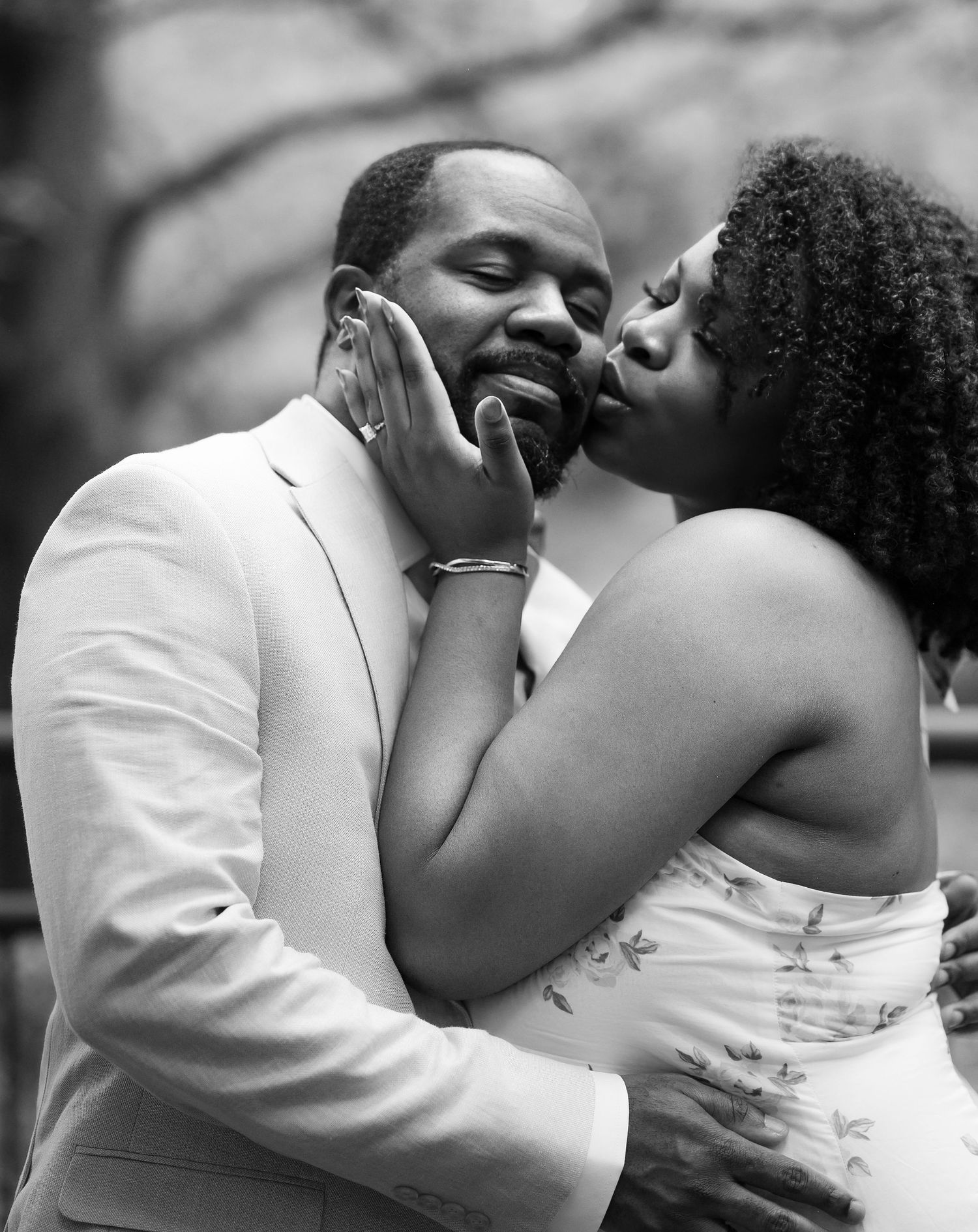 A tender black and white close-up of a woman kissing a mans cheek while cradling his face with her hand.