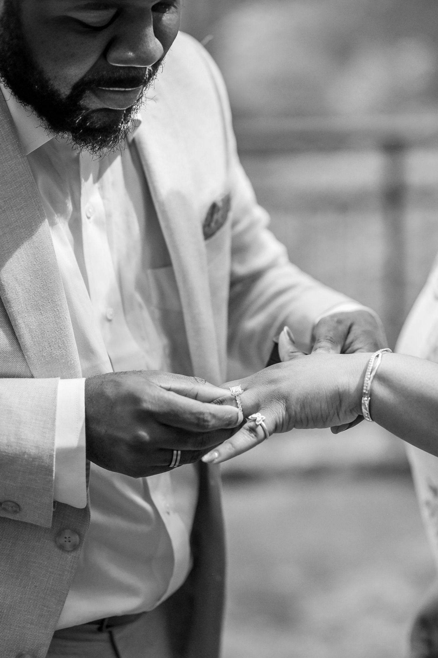 Close-up black and white photo of man placing engagement ring on womans finger during proposal.
