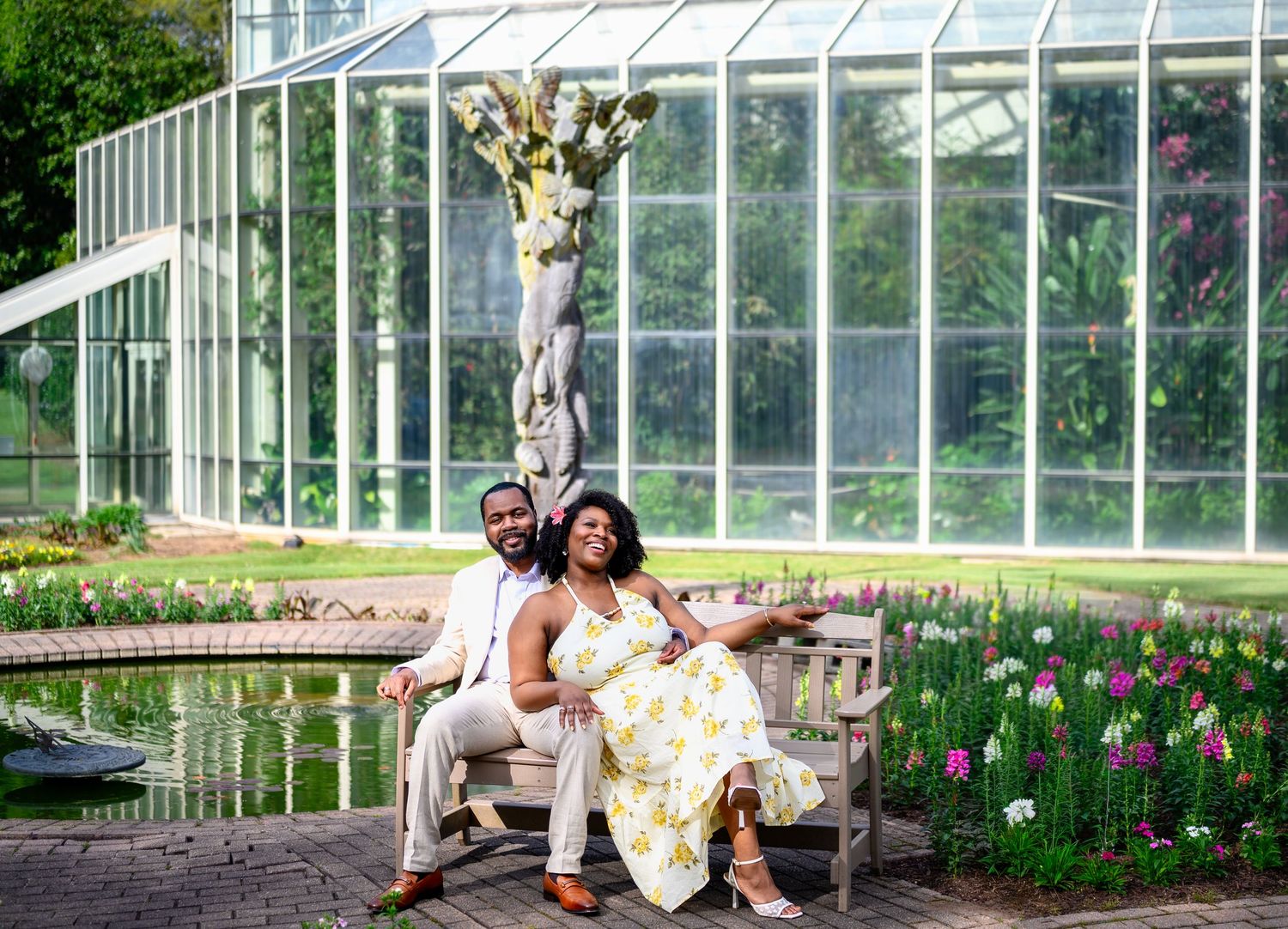 Couple posing on a garden bench in front of a greenhouse with tulips in bloom.