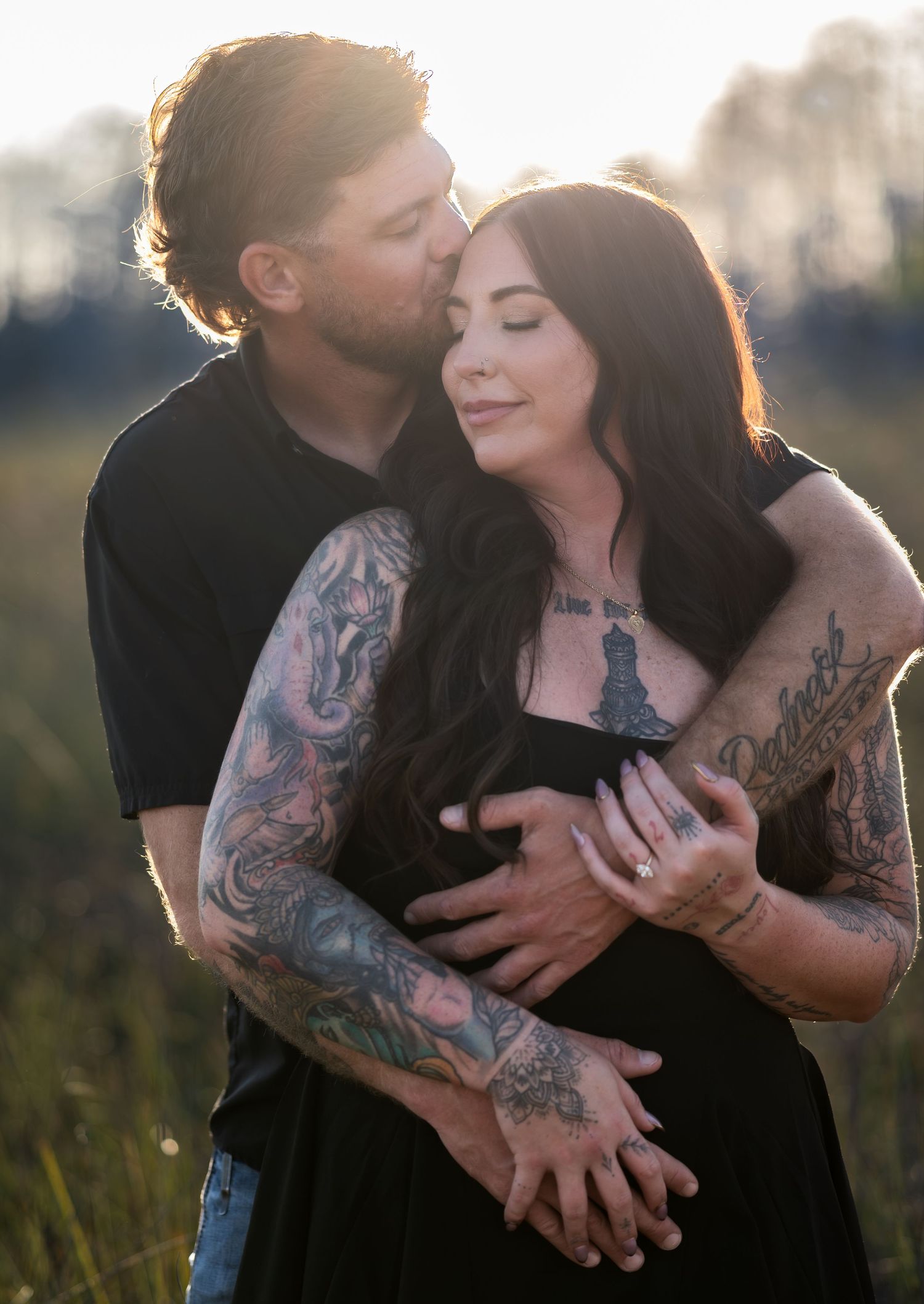 Couple shares intimate moments in golden sunlit field with visible tattoos.
