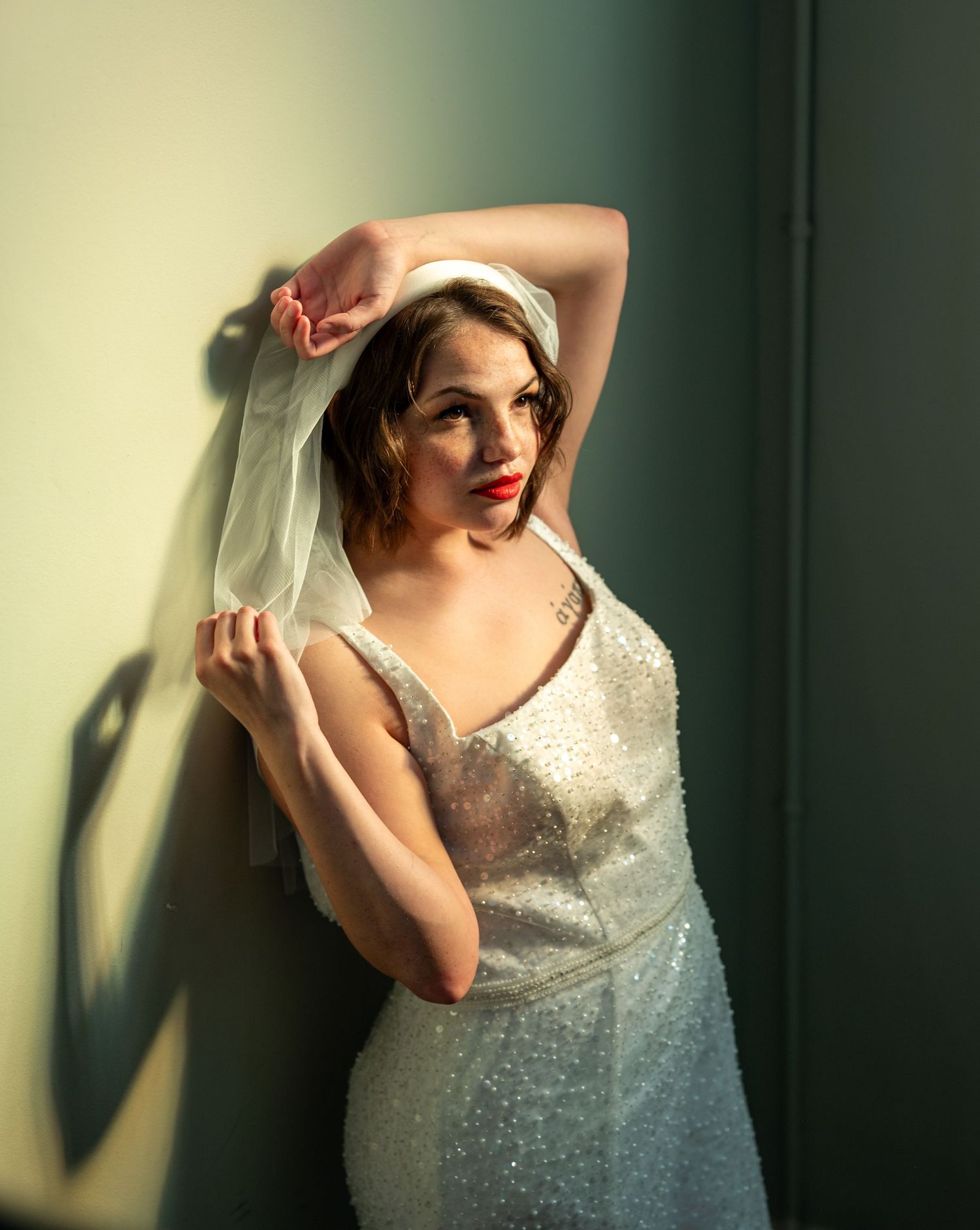 A figure in a beaded white wedding dress is photographed in an artistic sequence against a green wall with dramatic lighting.