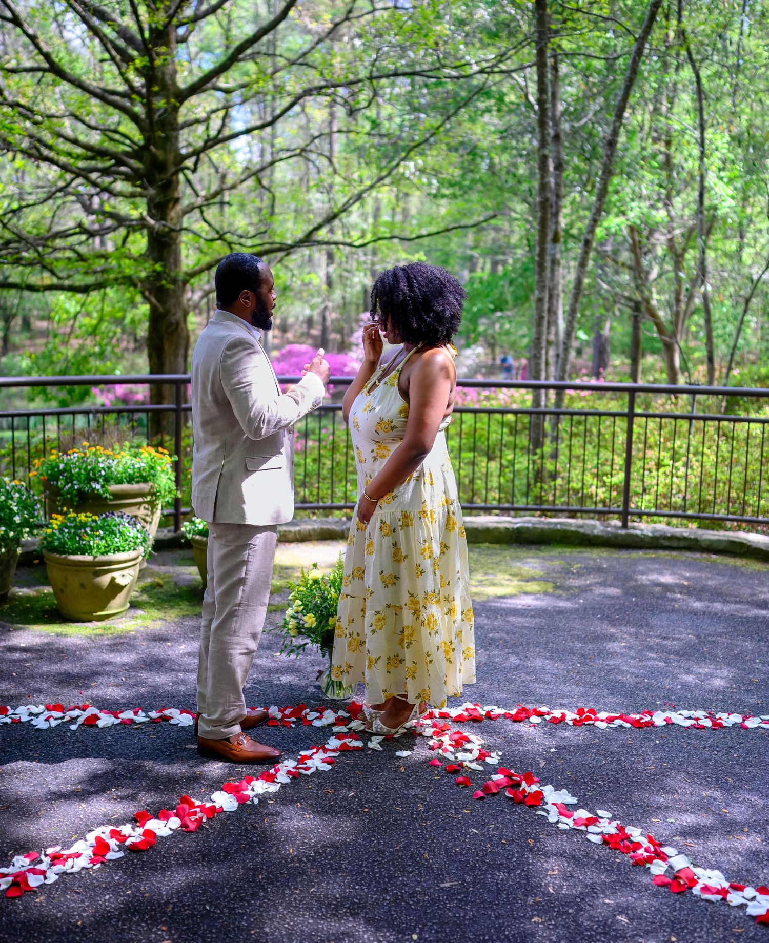 Couple standing on a petal-lined path in a lush green forest during a romantic marriage proposal.