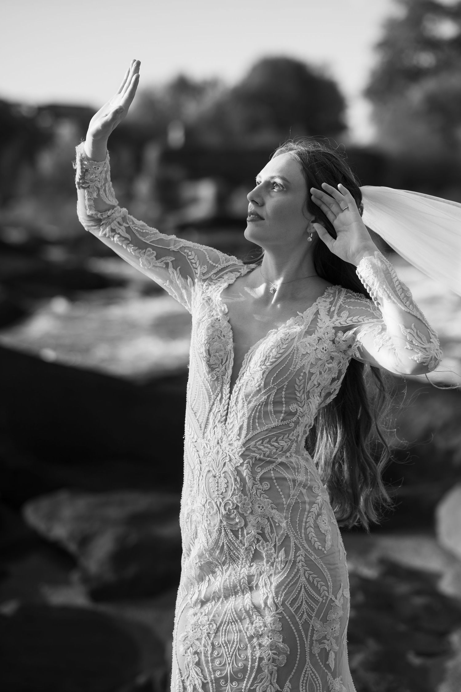 Black and white portrait of bridal pose in lace gown with dramatic veil movement.