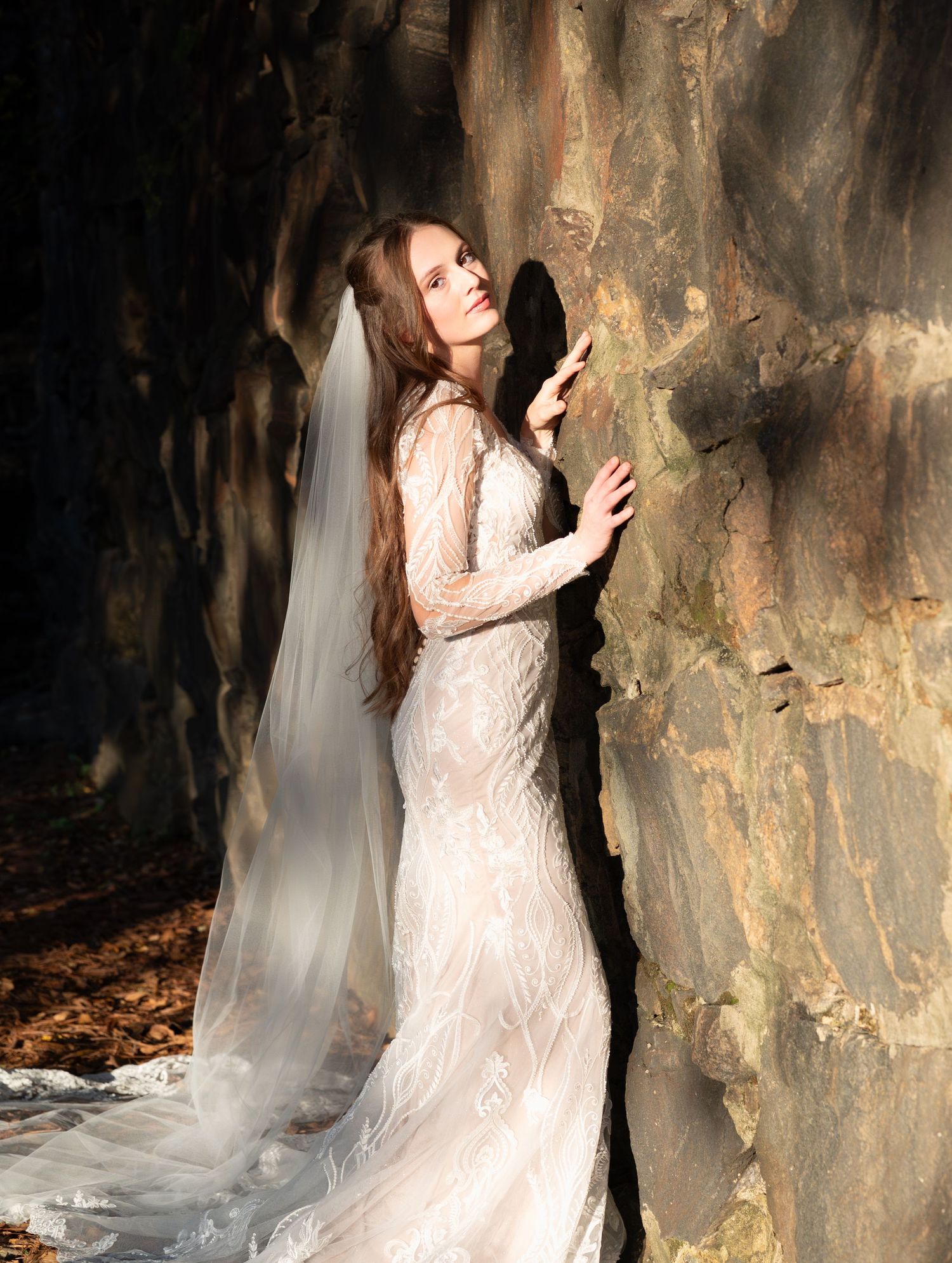 A moody bridal portrait series against textured stone walls with dramatic lighting and flowing veil.