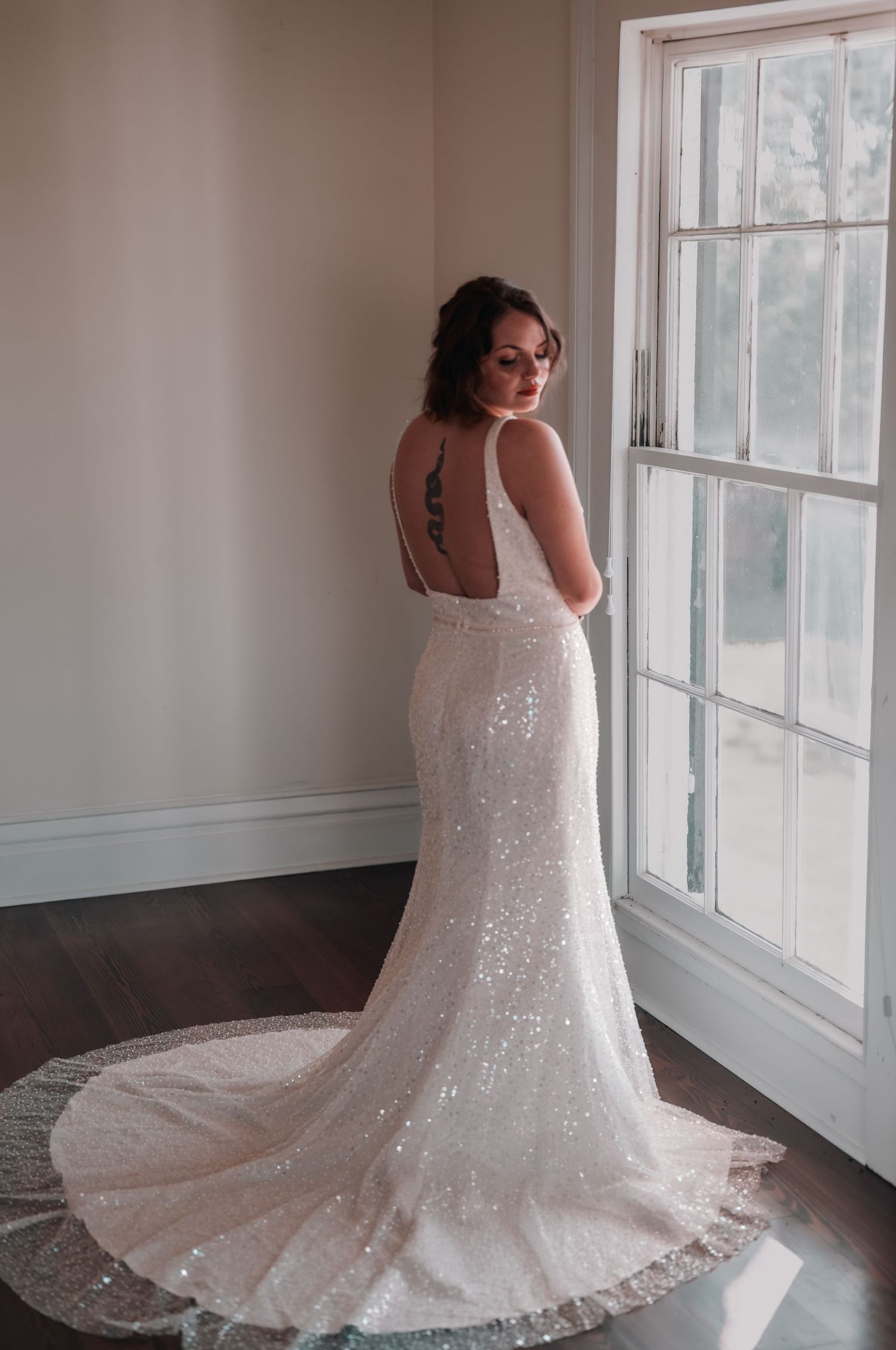 A stunning sequined white wedding dress with a long train is showcased in a bright, sunlit room.
