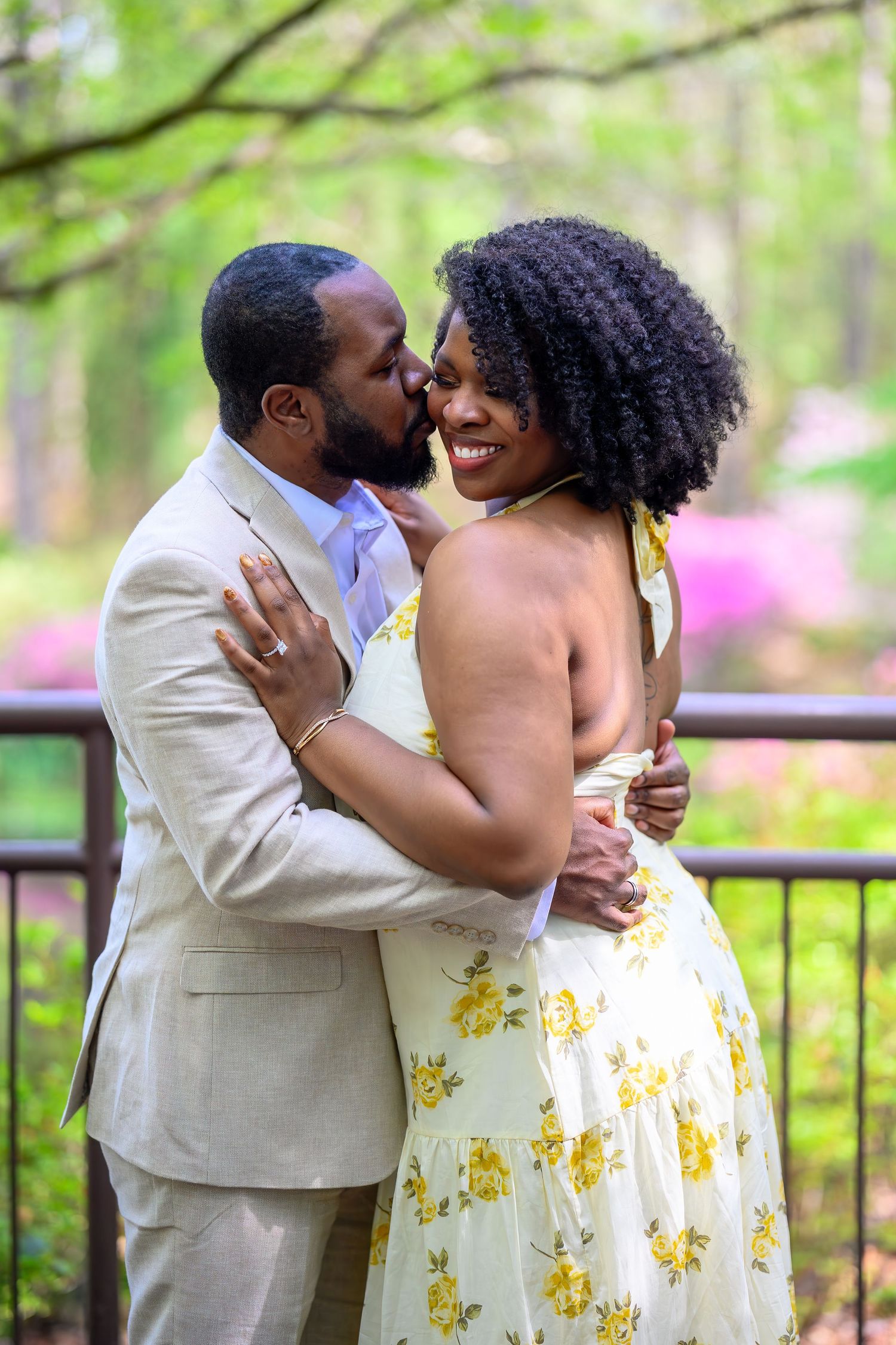 Groom kissing smiling bride on cheek in lush green garden setting.
