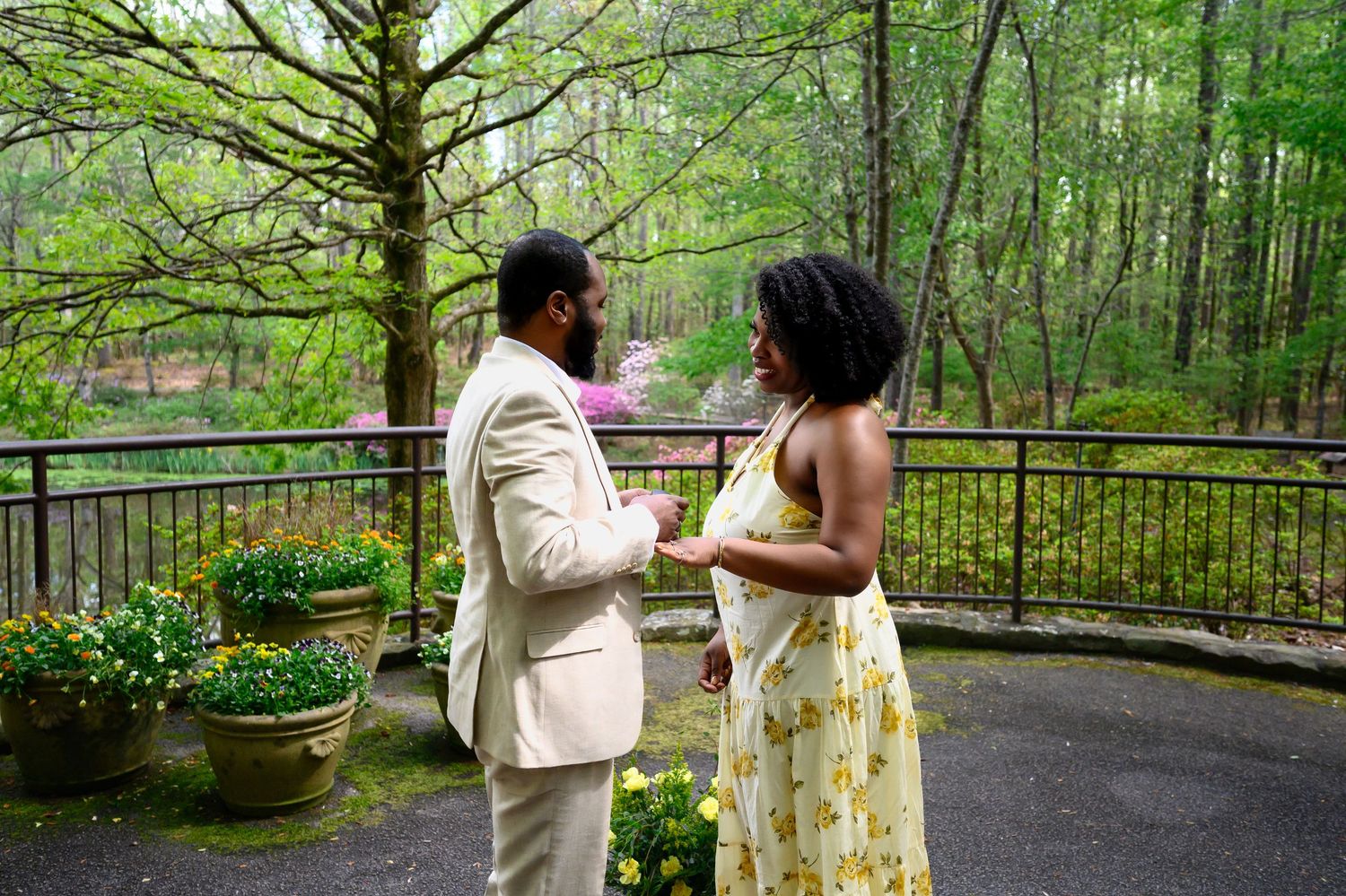 A couple shares a romantic moment on an outdoor terrace surrounded by blooming spring flowers and lush green trees.