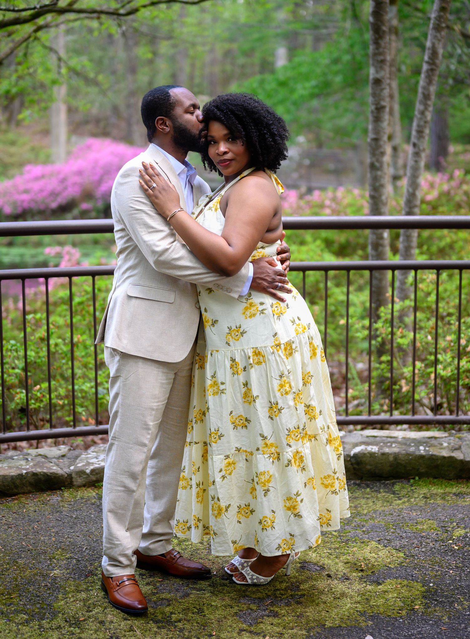 Couple embracing and kissing in garden with blooming azaleas backdrop.