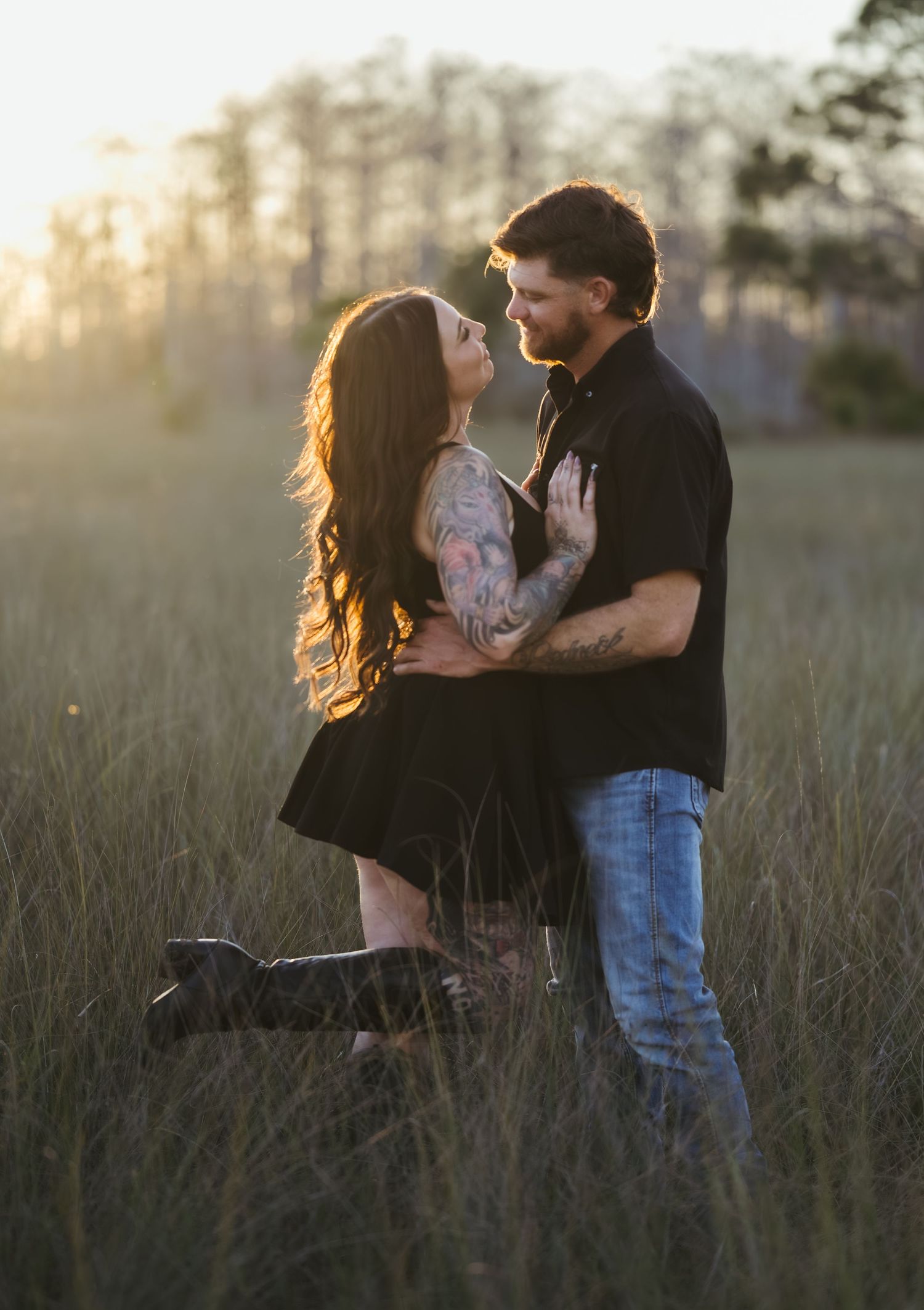 Romantic couple embraces in tall grass field during golden hour sunset.