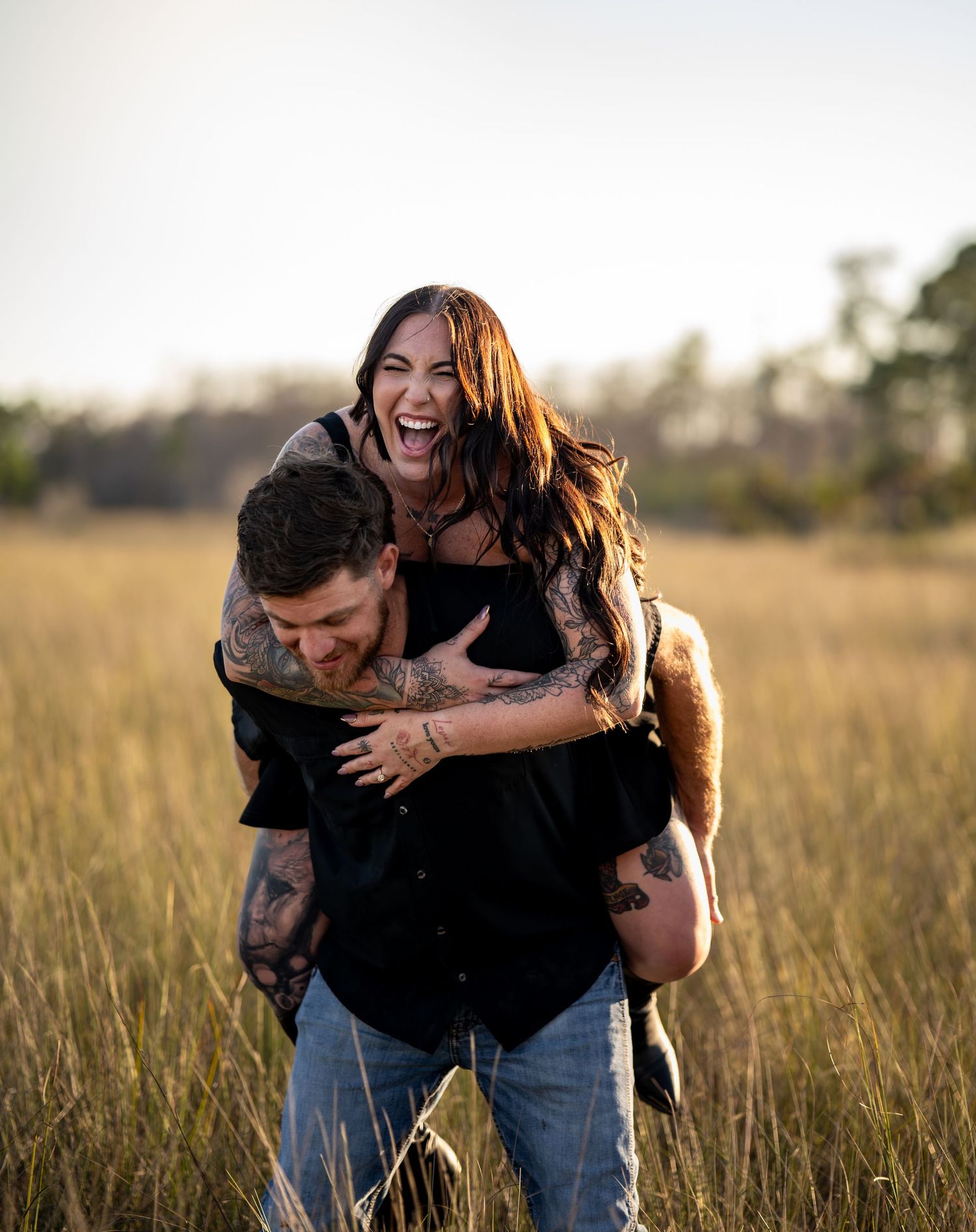 Joyful couple playing and laughing in a sun-drenched field at dusk.