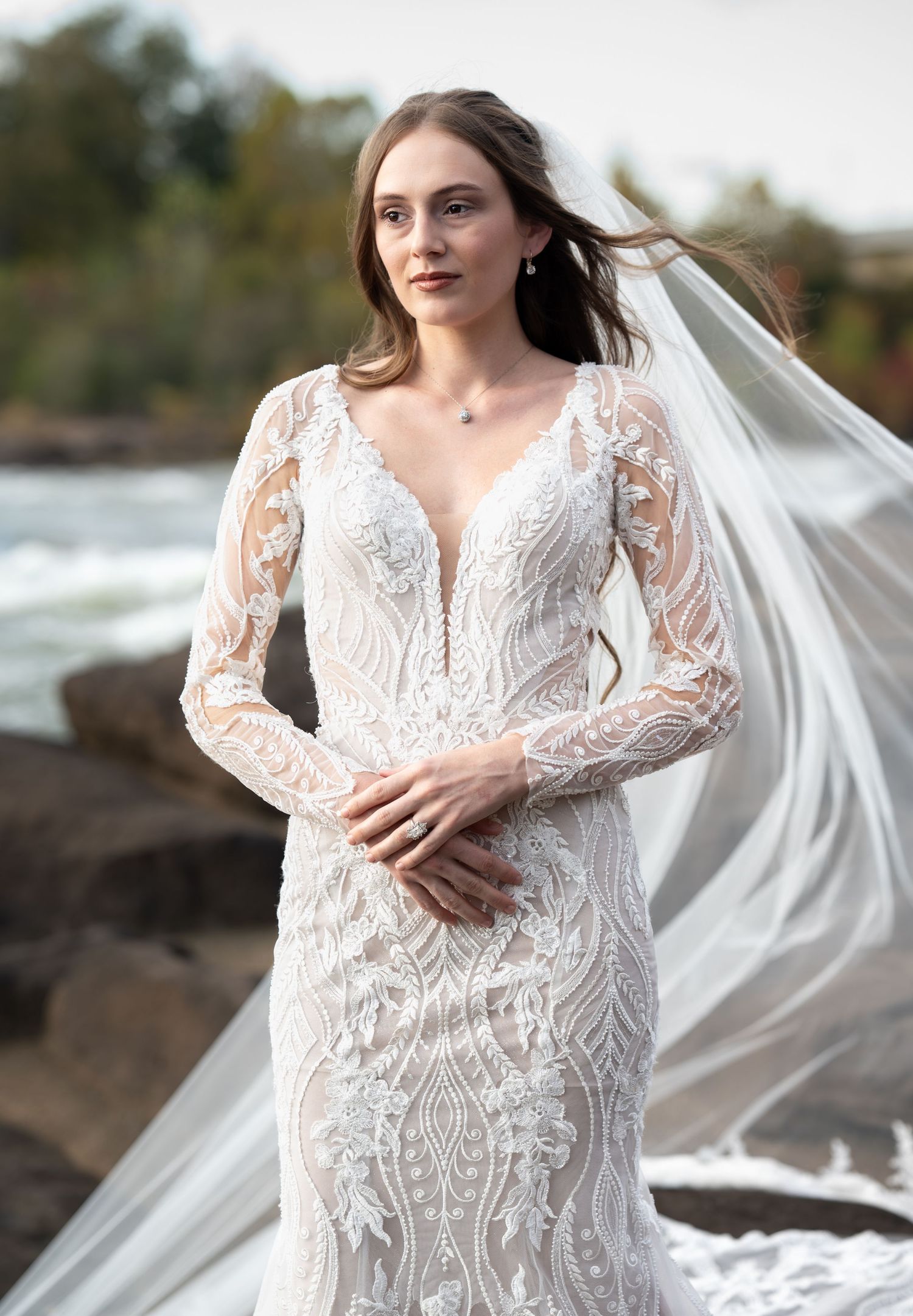 A detailed lace wedding dress with long sleeves photographed against a cloudy sky.