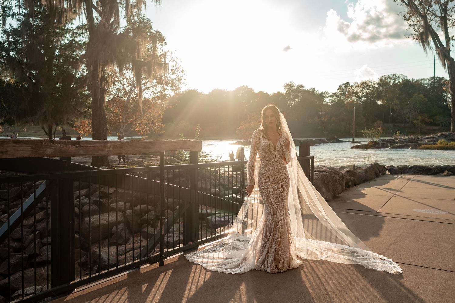 Golden sunlight illuminates a bride's silhouette against metal railings at sunset.
