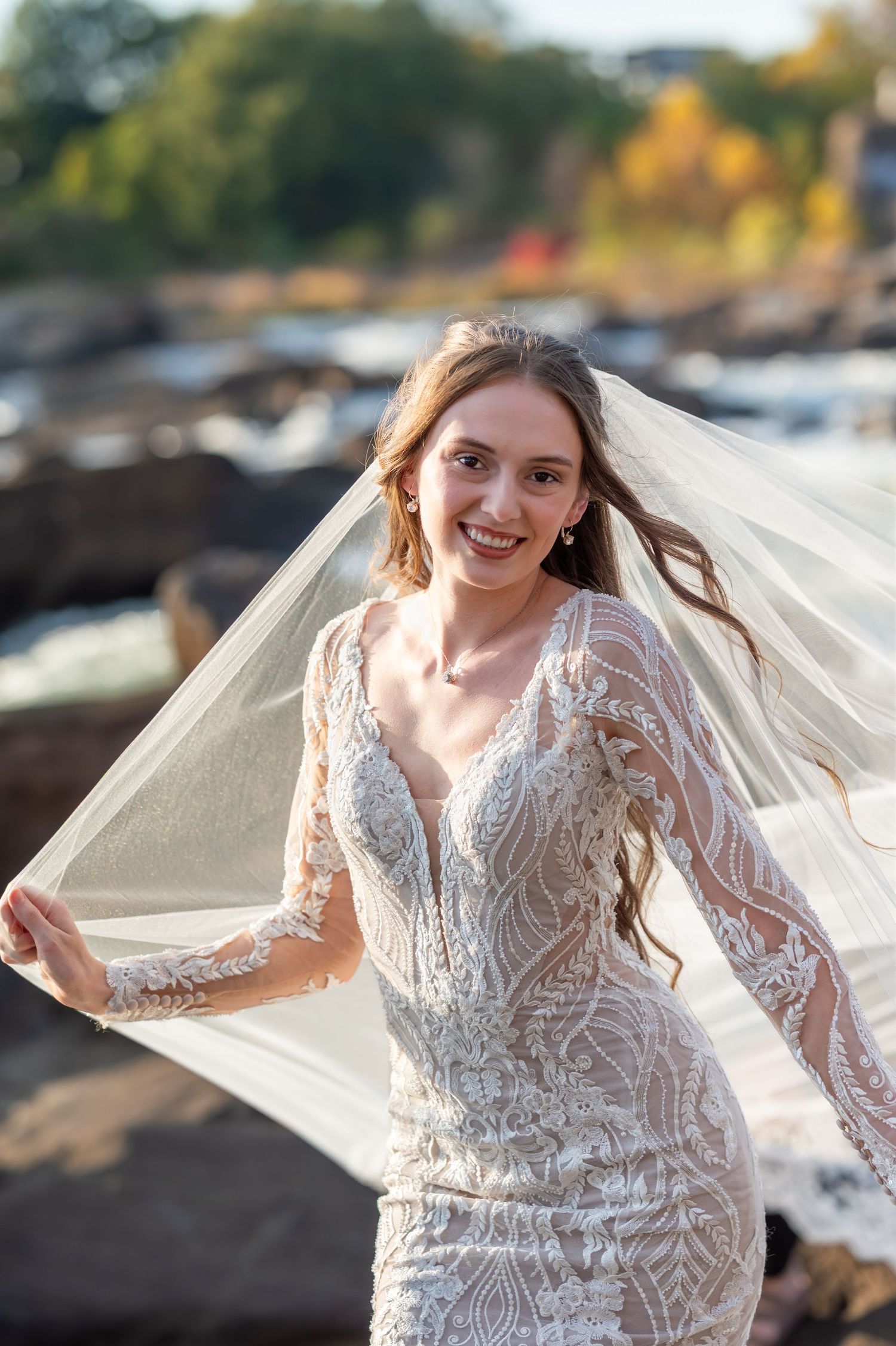 Joyful bridal portrait with cathedral veil catching sunlight on rocky outdoor setting.