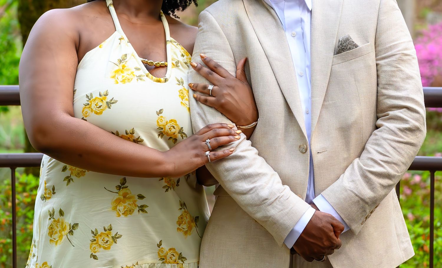 Close-up of newly engaged couple showing off ring, woman in yellow floral dress, man in tan suit.