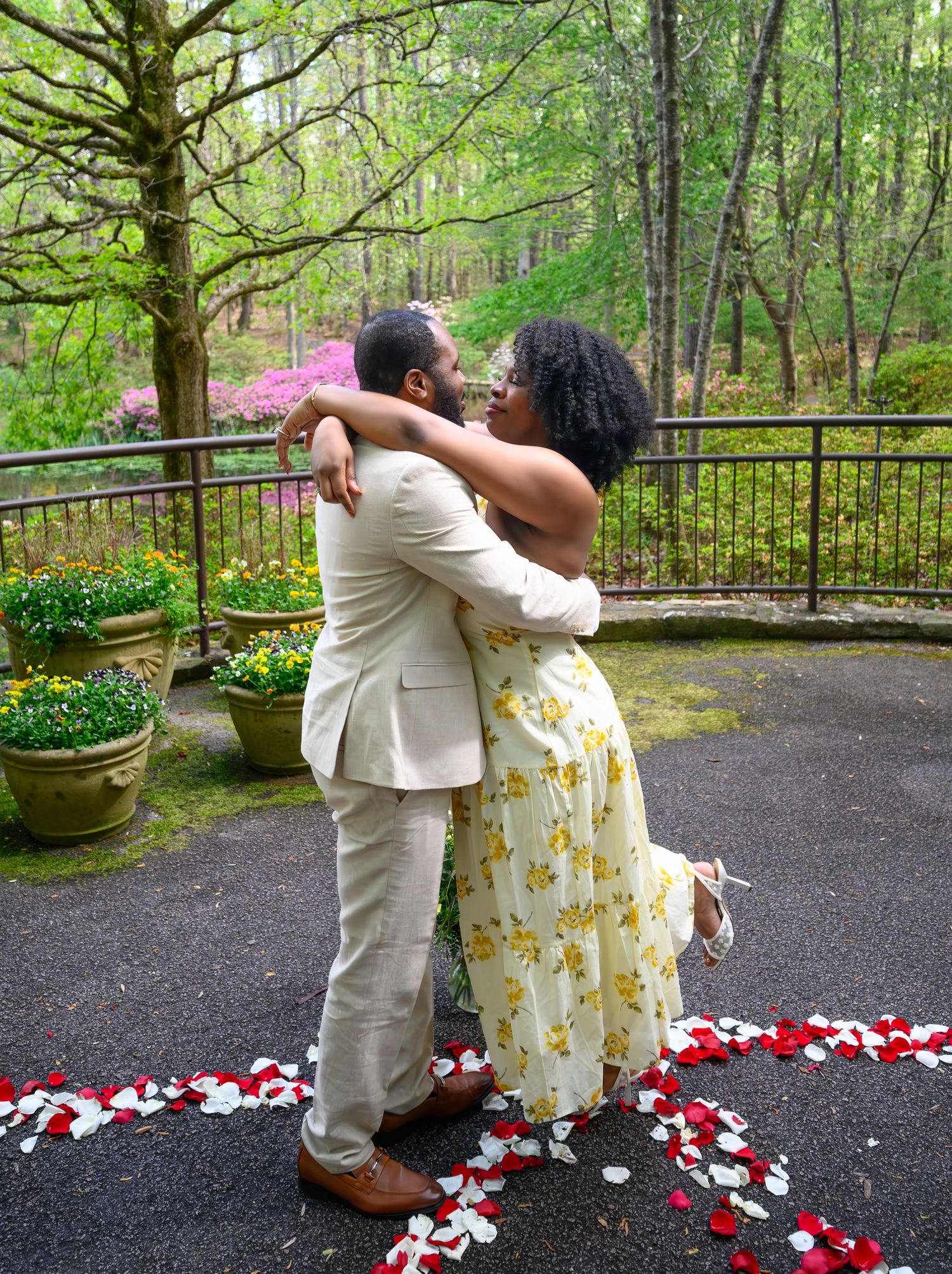 A couple embraces tenderly on a petal-lined path in a lush garden during their engagement session.