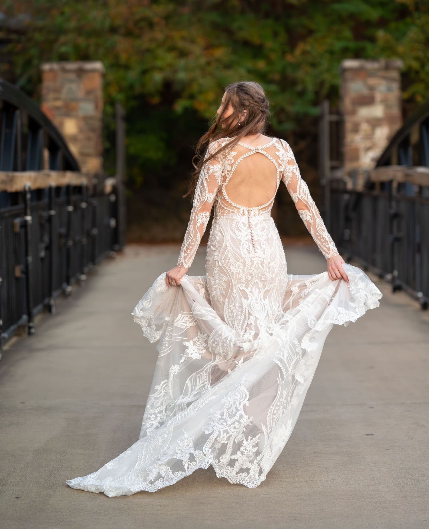 Back view of bride in open-back lace gown twirling dress on bridge walkway.
