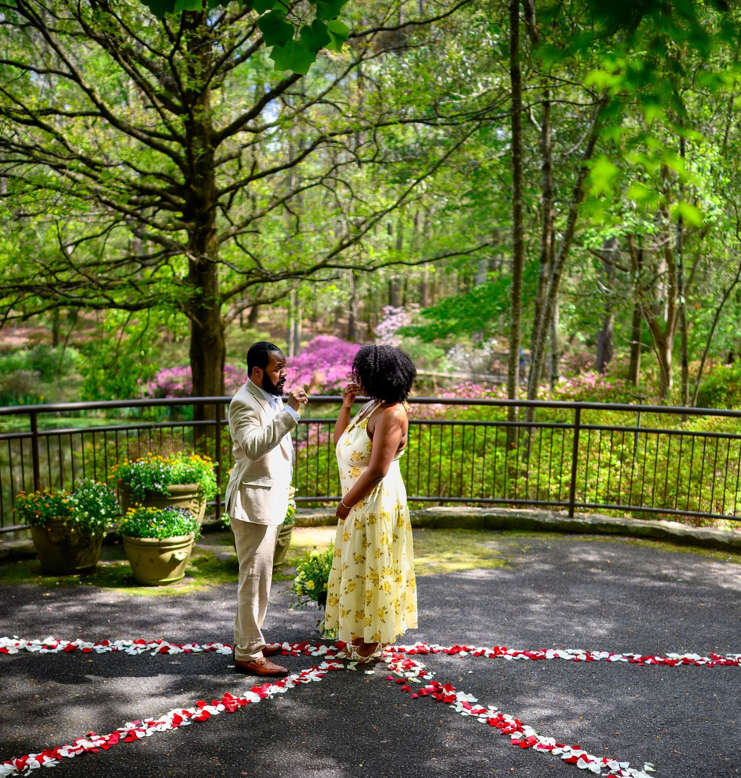 Couple stands together on rose petal heart design during romantic outdoor proposal in spring garden.
