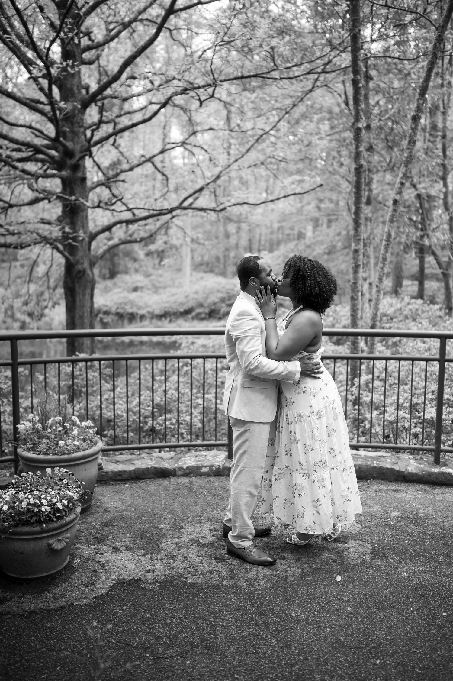 Black and white photo of couple sharing a romantic kiss on an outdoor terrace surrounded by trees.