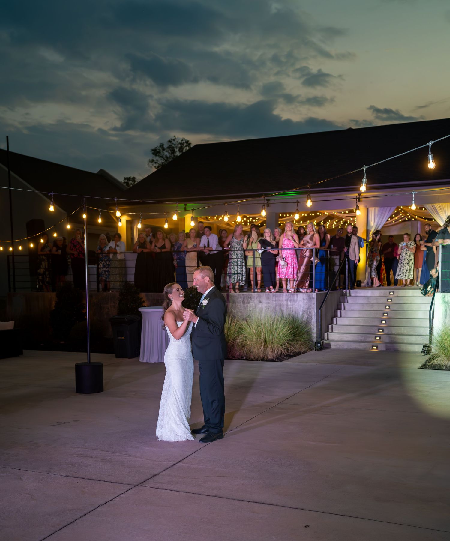 Wedding reception dance floor at night with string lights and silhouettes of guests dancing.