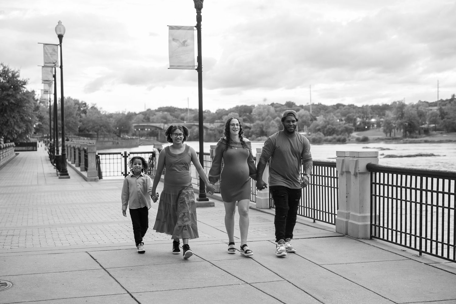 A sequence of people walking along a waterfront boardwalk on an overcast day.