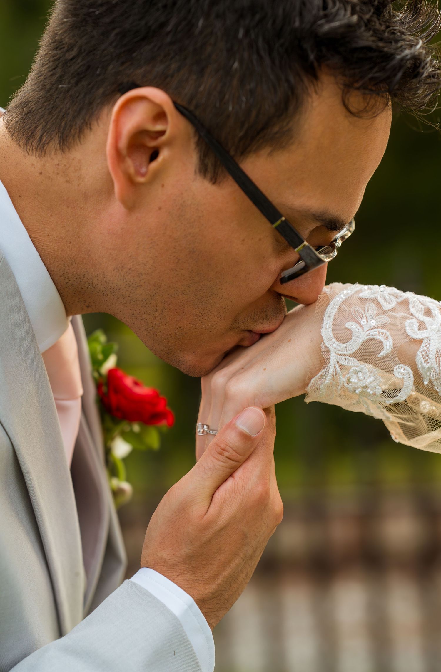Groom in grey suit wipes tears away during an emotional moment at an outdoor wedding ceremony.