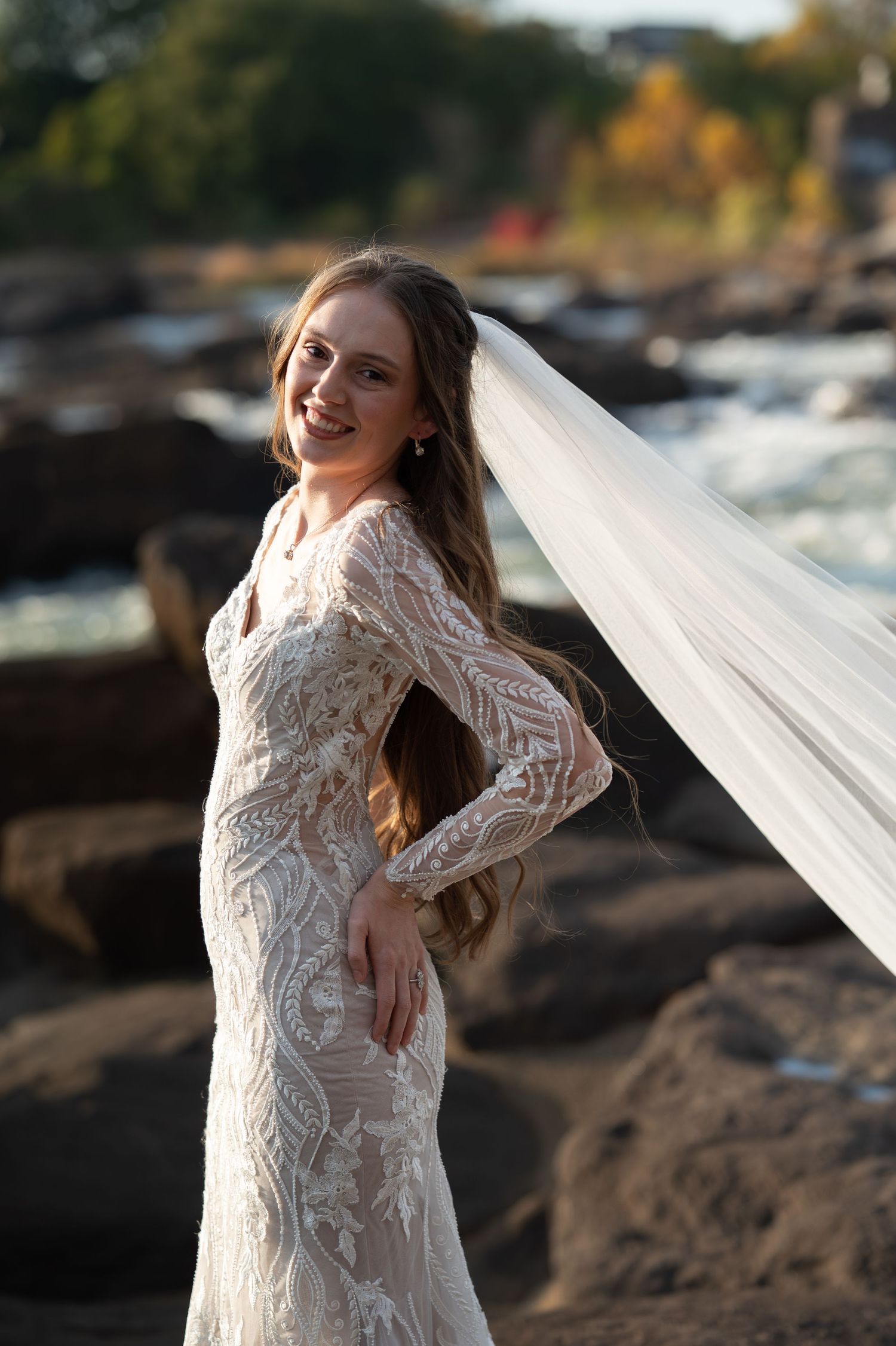 Artistic bridal portrait with long-sleeved lace gown against rushing water backdrop.