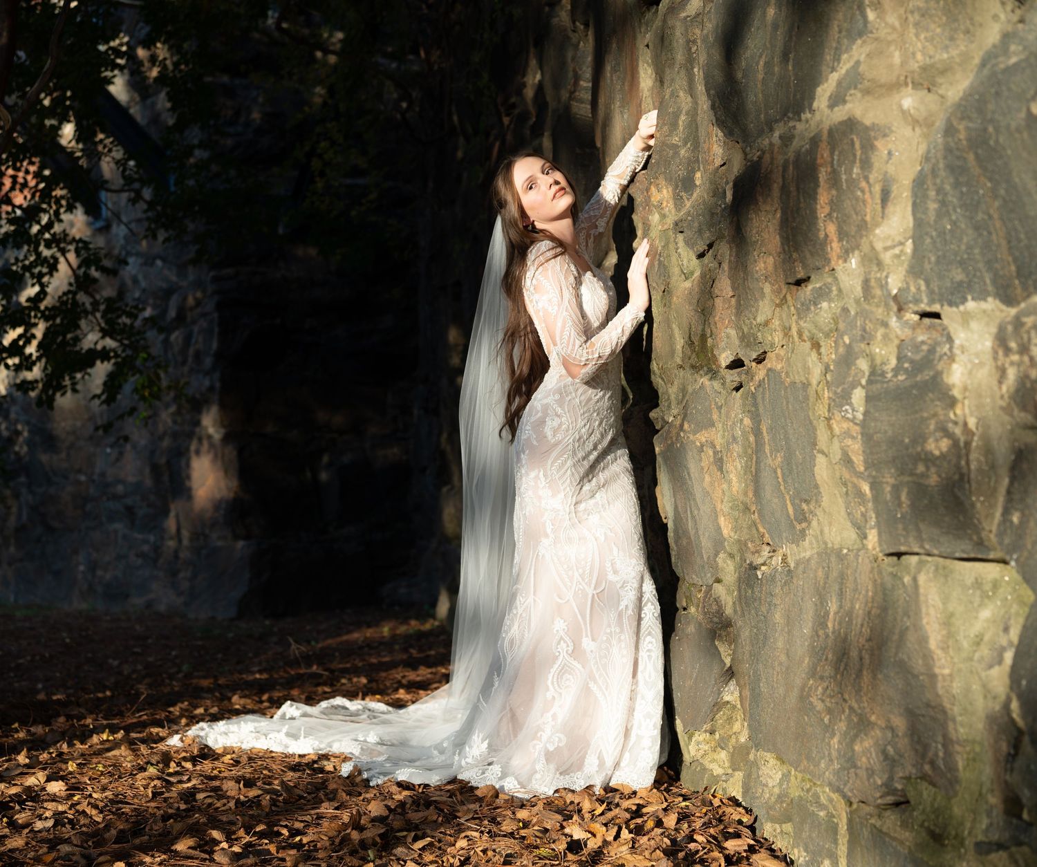 Ethereal bridal portrait against stone wall with long veil in autumn setting.