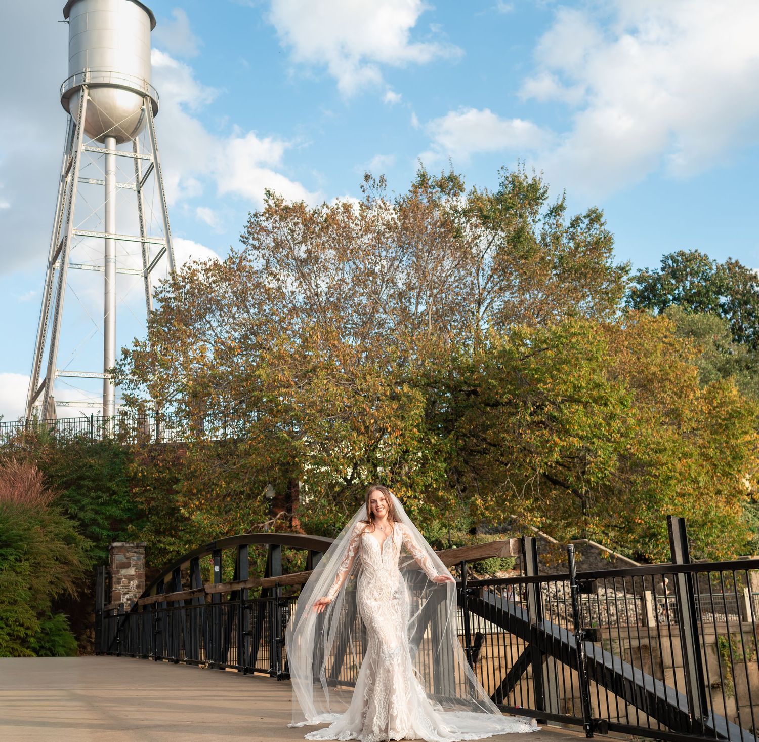 Wedding dress photographed near white water towers surrounded by autumn trees.