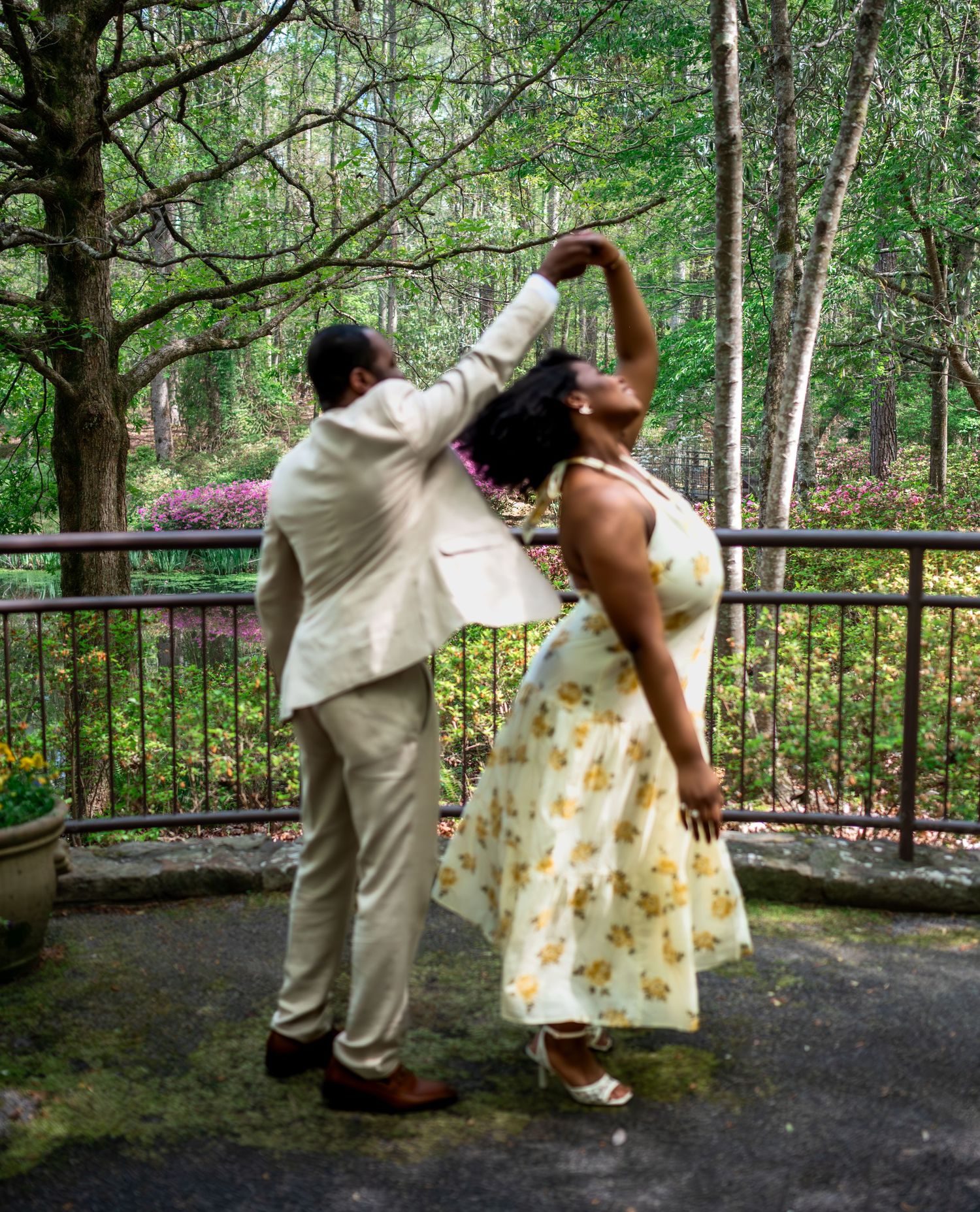 A joyful couple dances together outdoors in a green garden setting, the man spinning the woman gracefully.