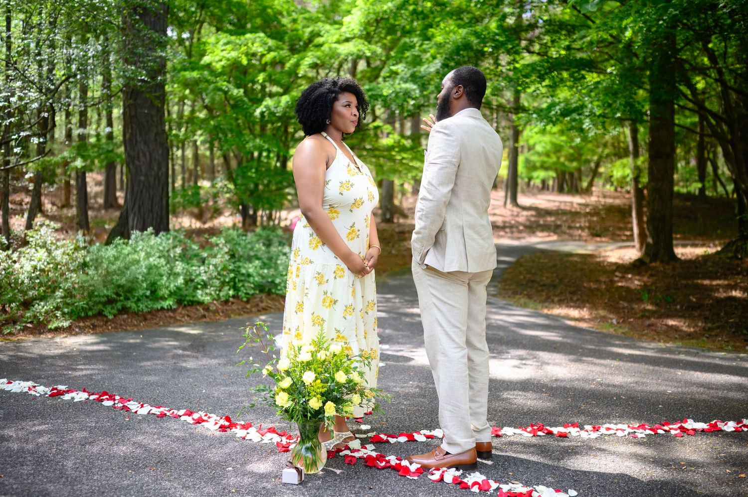 Man and woman facing each other on a tree-lined path decorated with red and white rose petals.