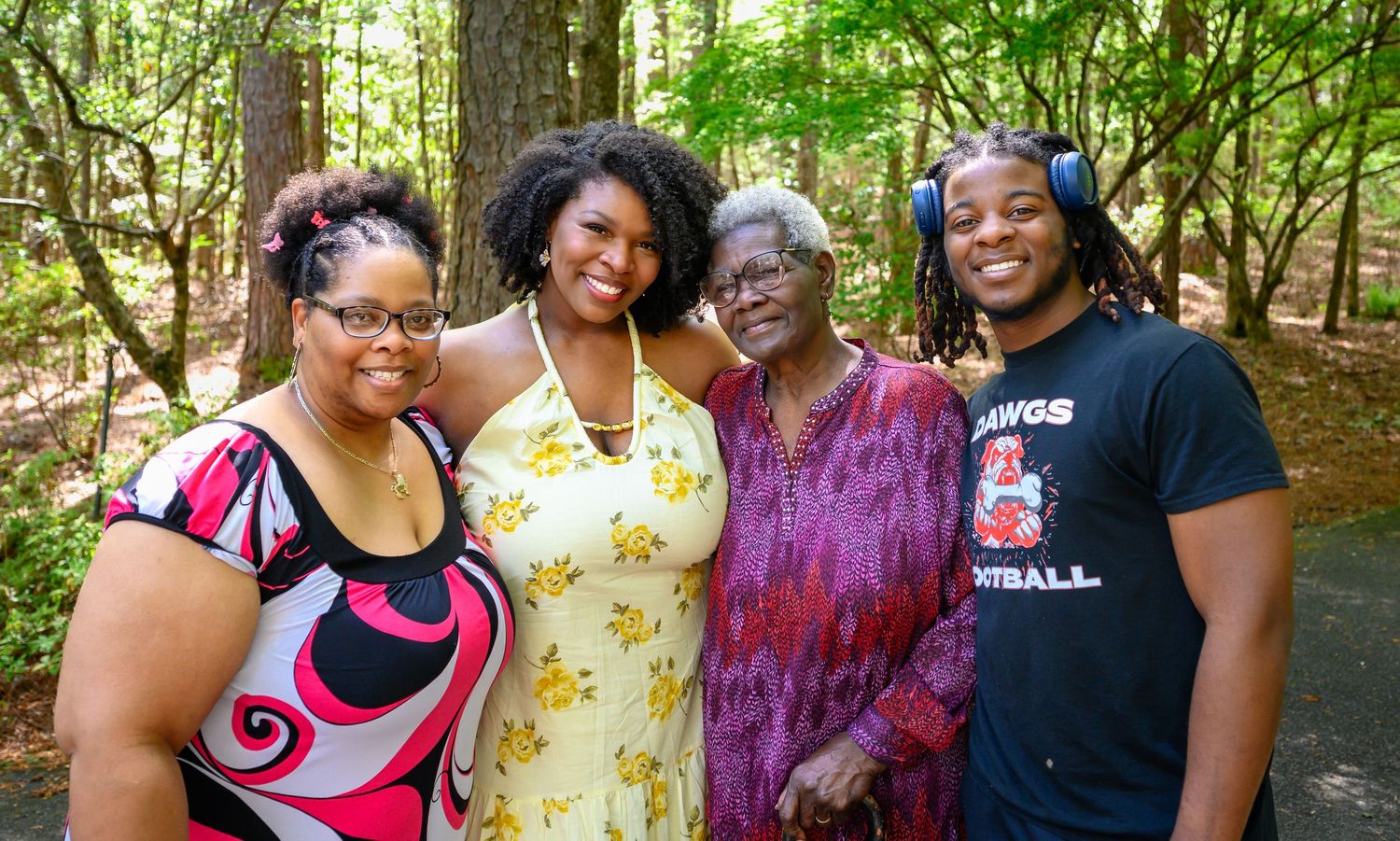 Four generations of women posing together outdoors in a lush green woodland setting after a marriage proposal.