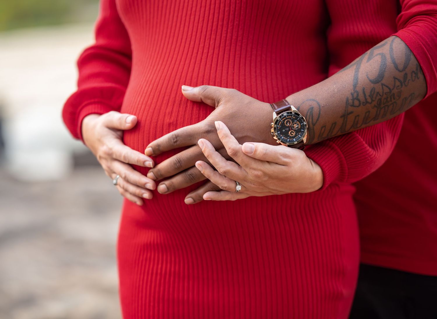 Close-up detail of hands and red sweater during an intimate outdoor photoshoot.