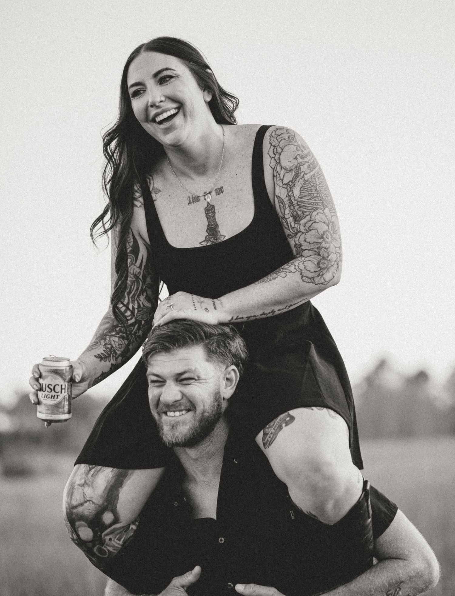 Black and white photo of a couple laughing together outdoors in a casual, candid moment.
